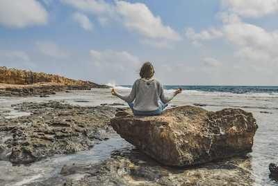 woman meditating on rock by sea